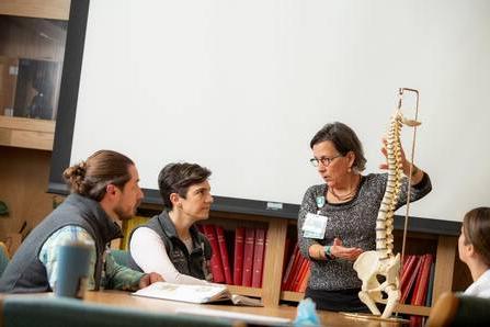 Instructor and 3 students with an anatomical spine  model in classroom